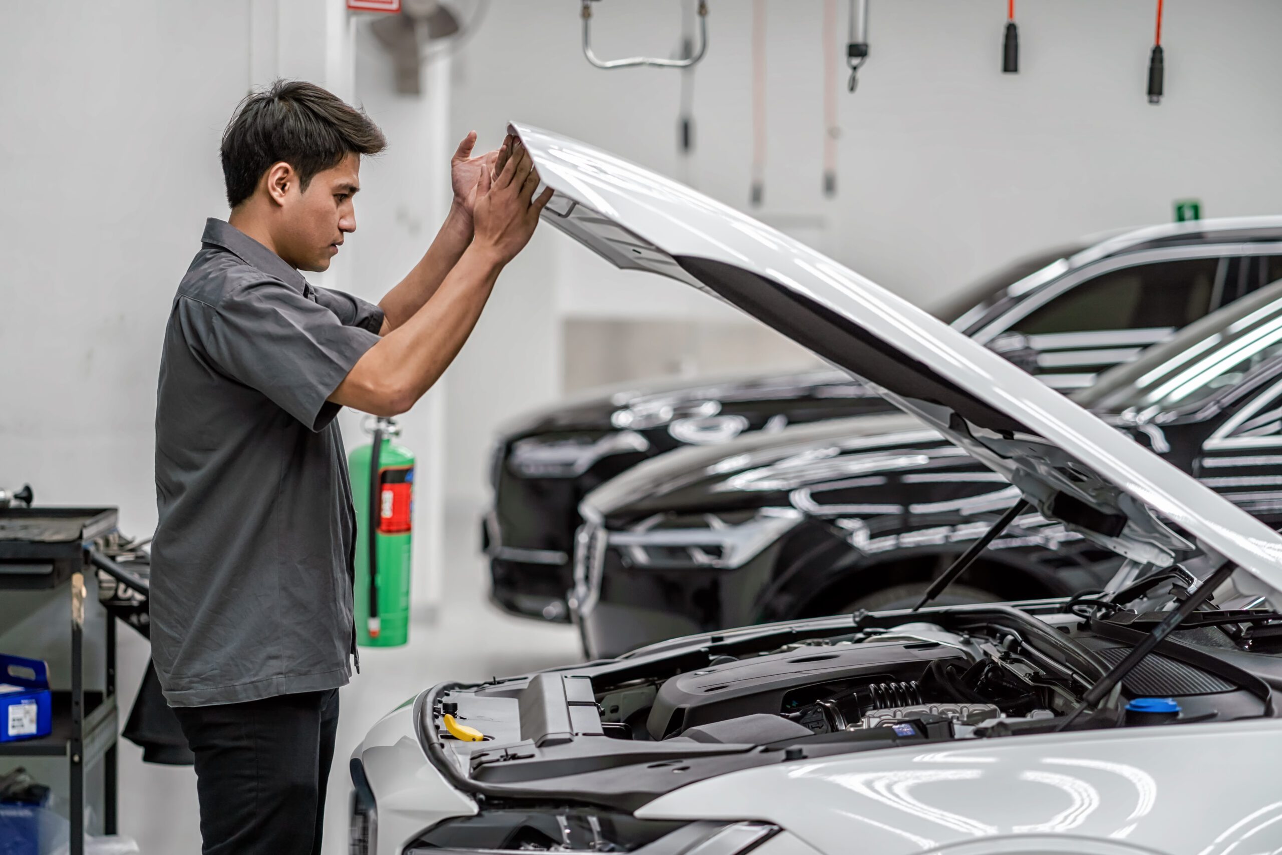 Asian mechanic Checking and Opening the car hood in maintainance service center which is a part of showroom, technician or engineer professional work for customer, car repair concept